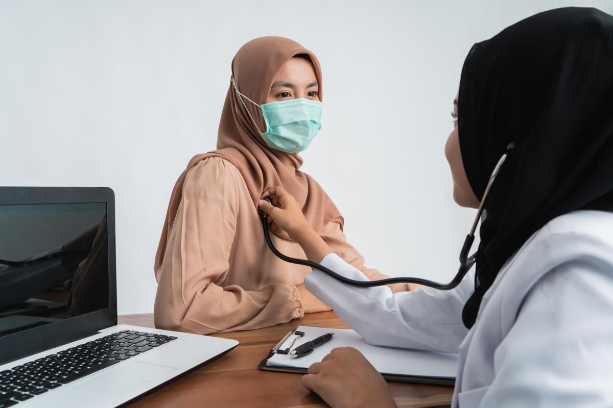 Wanita berjilbab dan bermasker sedang diperiksa dokter wanita berjilbab