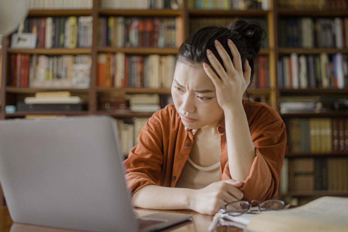 Wanita duduk termenung di depan laptop karena stres