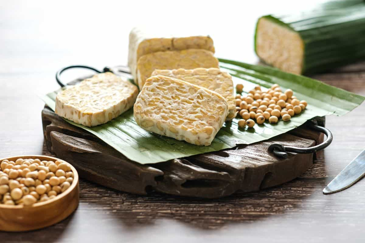 Potongan tempe mentah di atas talenan kayu dan daun pisang