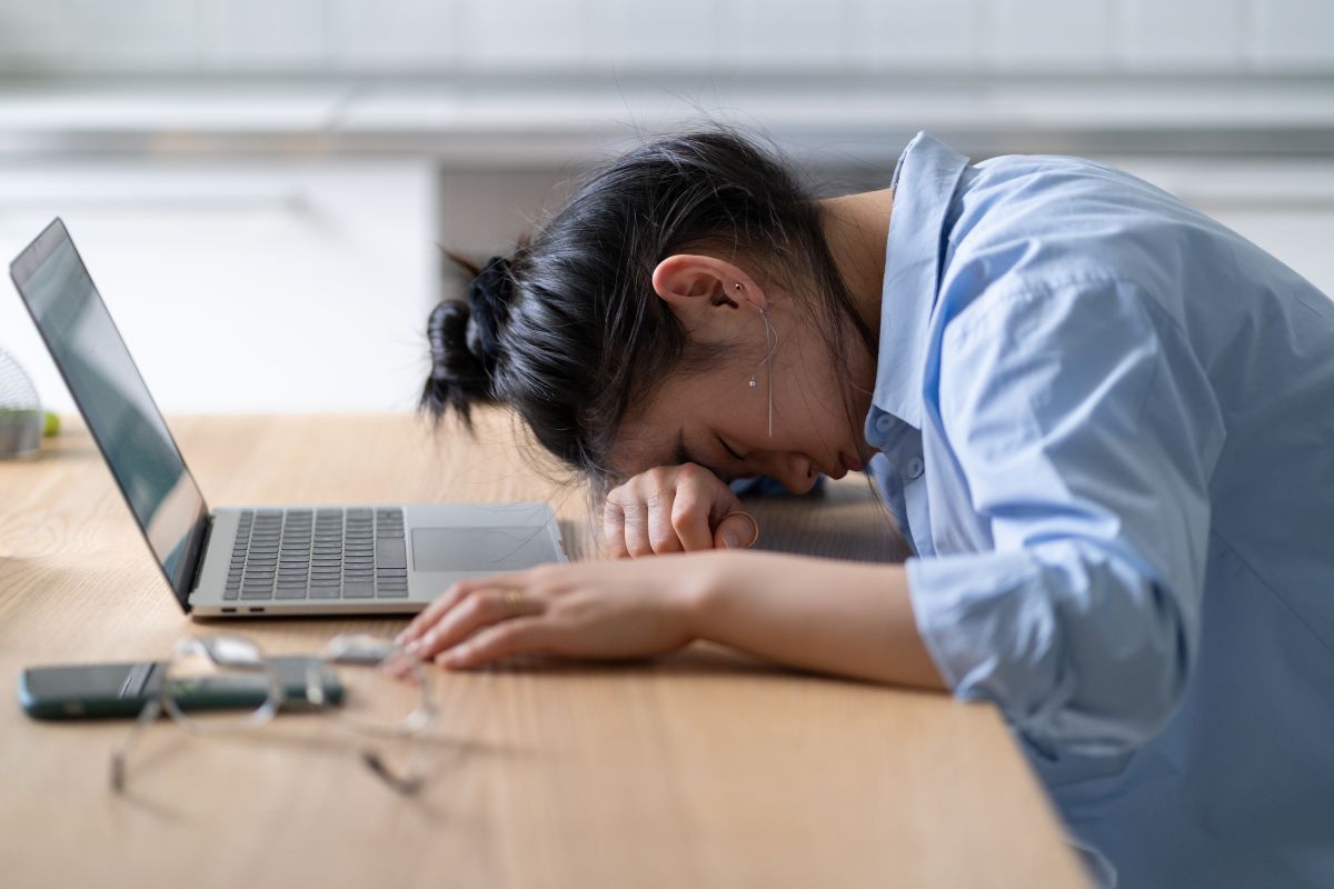 Seorang wanita tertunduk di depan laptop karena stres