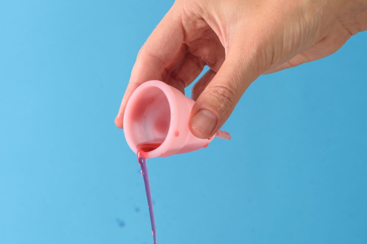 Tangan menuangkan cairan merah dari menstrual cup