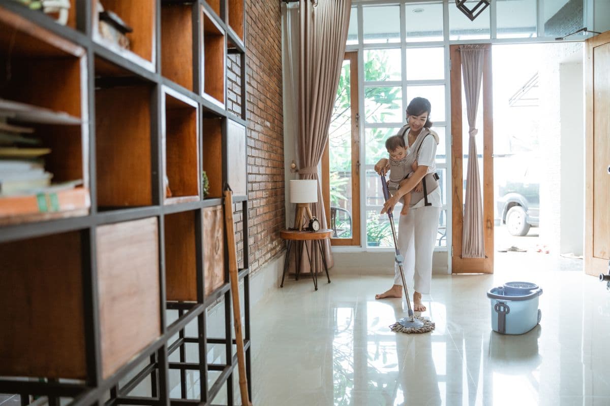 Seorang wanita sedang membersihkan rumah sambil menggendong bayi