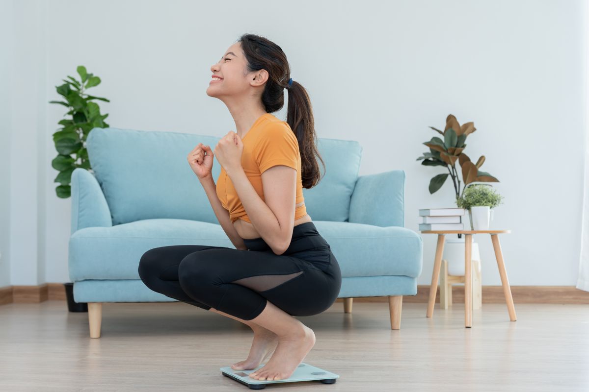 Wanita muda tersenyum bahagia saat melihat timbangan badan