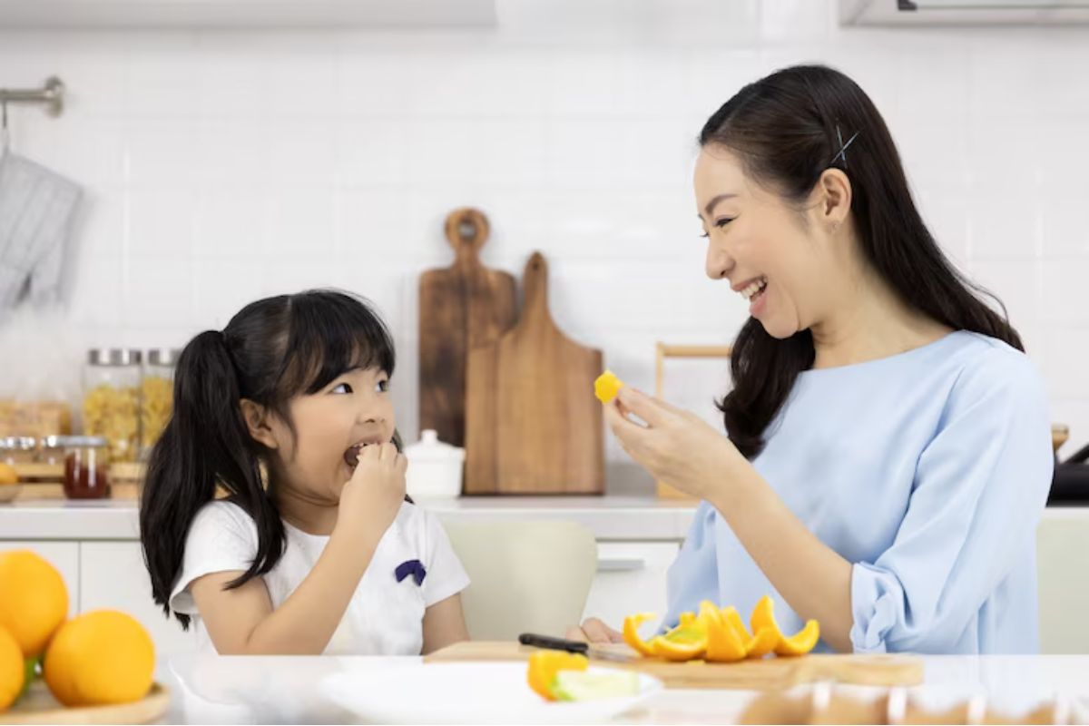 Ibu sedang makan jeruk bersama anak di dapur