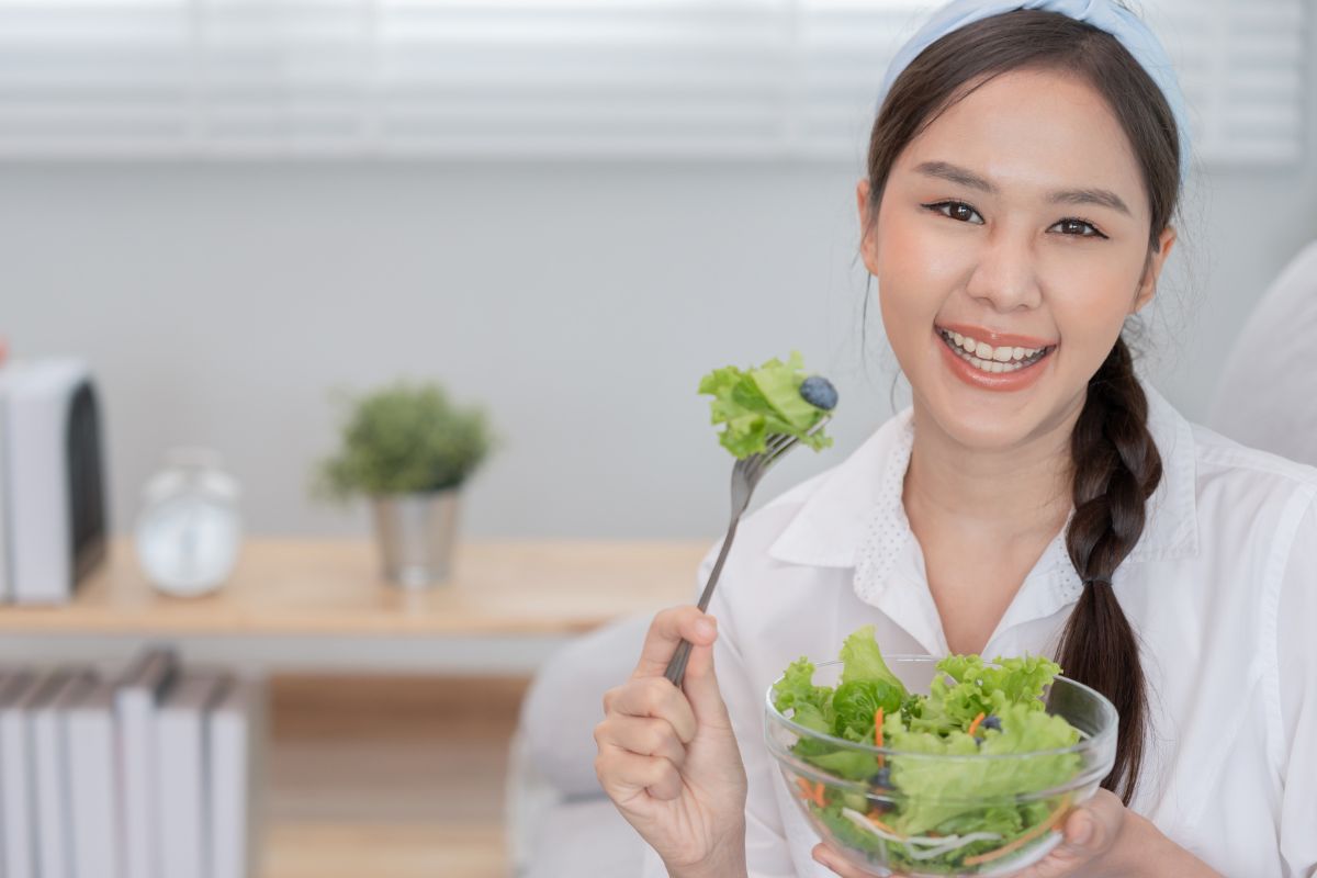 perempuan Asia tersenyum sambil makan salad