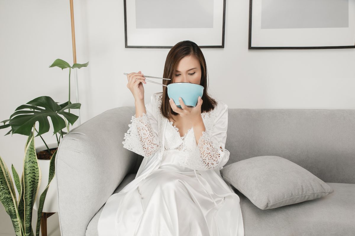 Wanita muda sedang duduk di sofa sambil makan