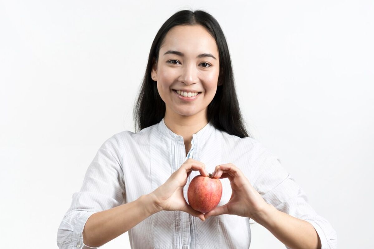 Wanita sedang memegang buah apel di depan jantung