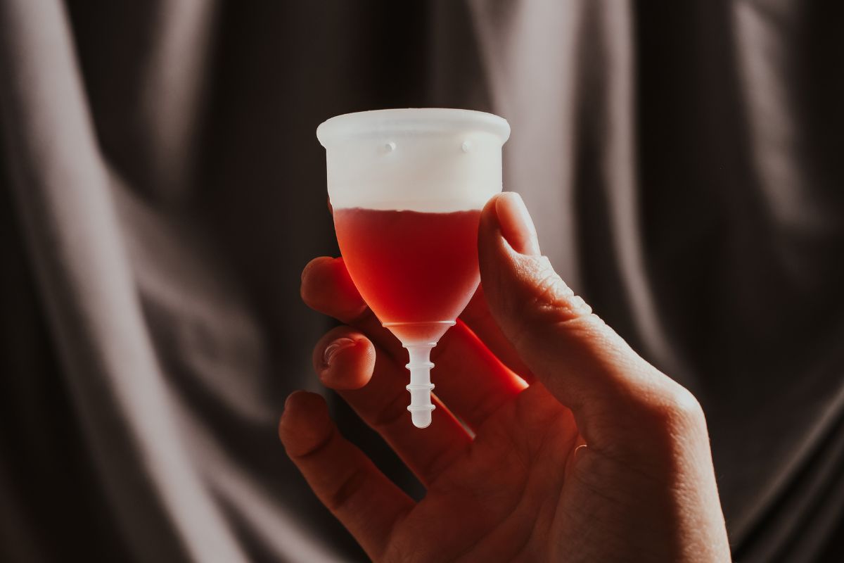 Tangan memegang menstrual cup dengan isi cairan merah