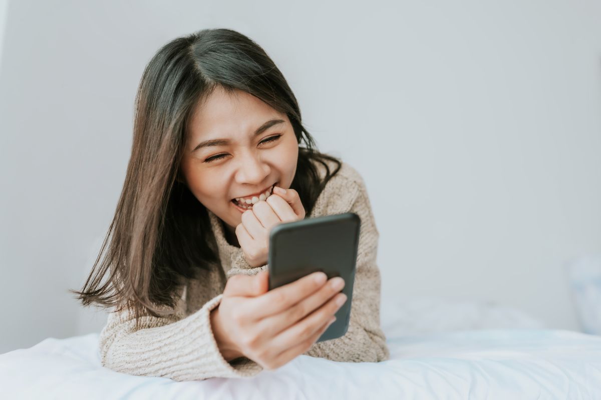 Wanita bermain ponsel di tempat tidur