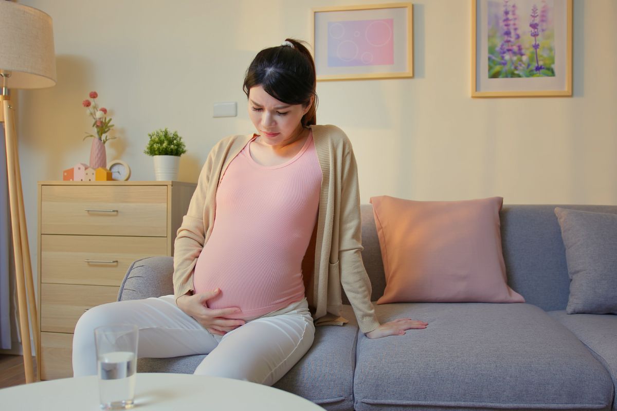 Wanita hamil sedang duduk kesakitan di atas sofa