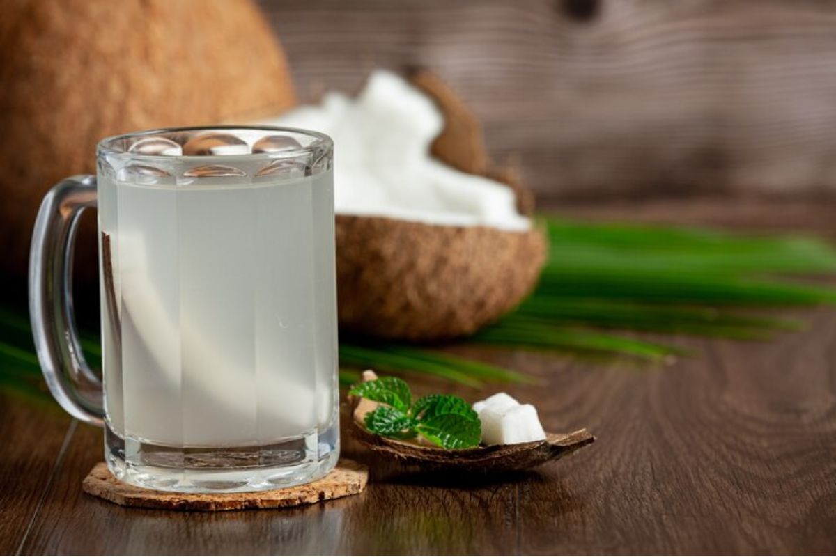 Segelas besar air kelapa dengan background batok kelapa