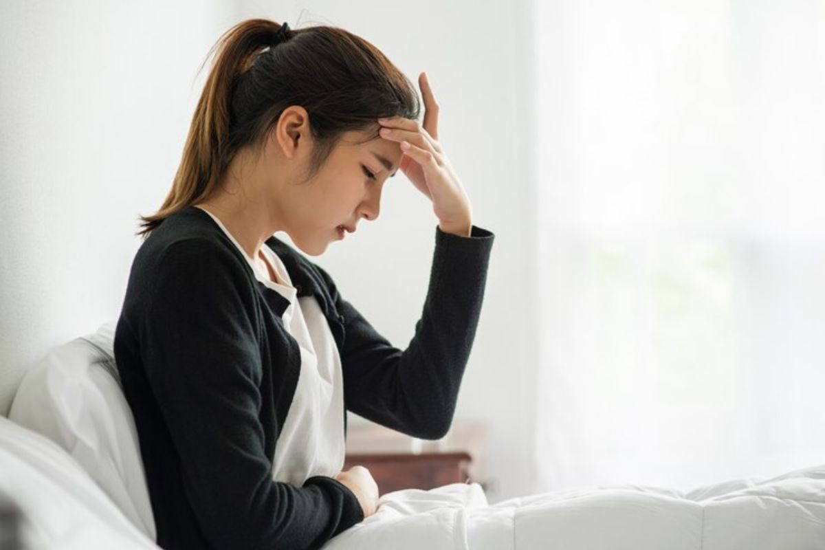 seorang wanita duduk di tempat tidur dan pusing karena anemia