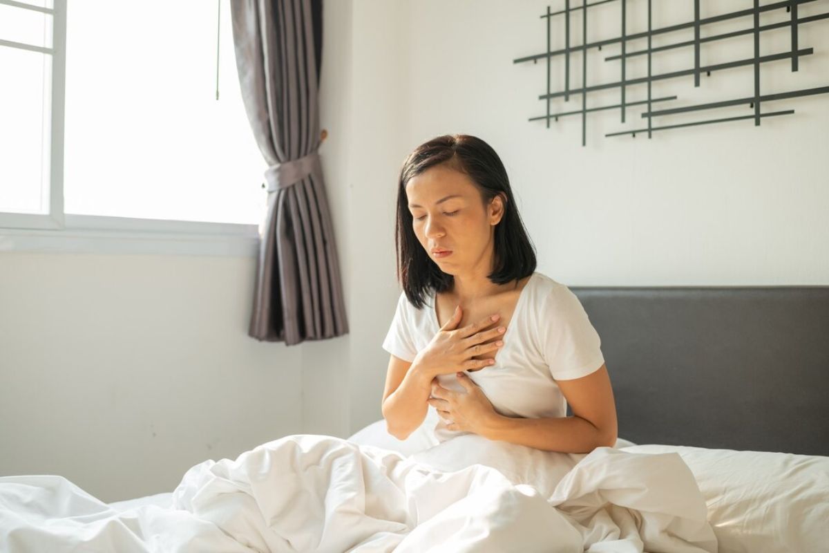 Perempuan duduk di tempat tidur merasa tidak nyaman