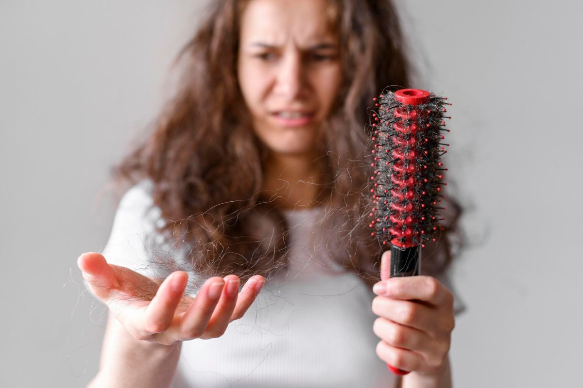 Seorang wanita memegang sisir dan rambut yang rontok karena kekurangan vitamin C