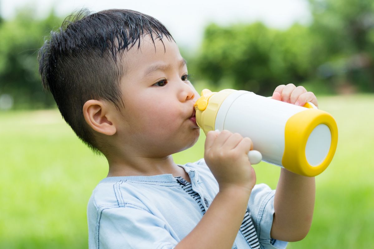Anak kecil laki-laki sedang minum dari botol plastik