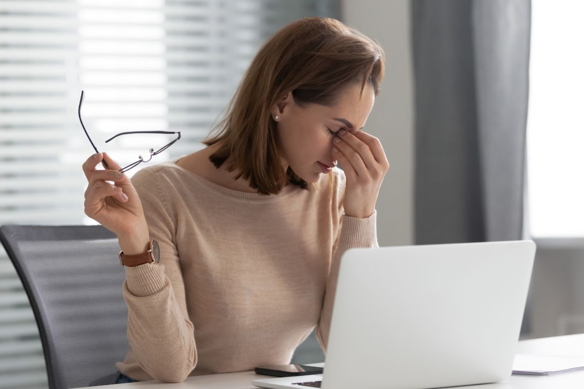 Seorang wanita yang sedang bekerja depan laptop merasa pusing dan memegang pelipisnya