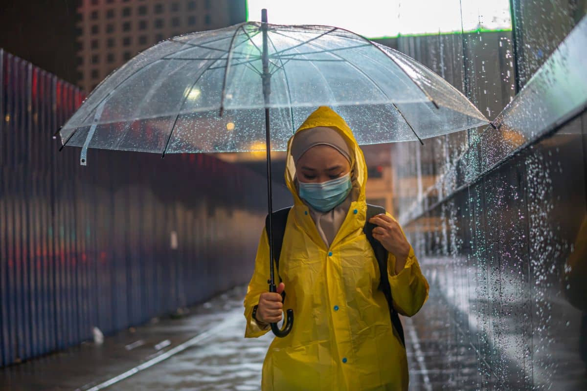 Orang yang sedang menggunakan jas hujan sekaligus payung saat hujan