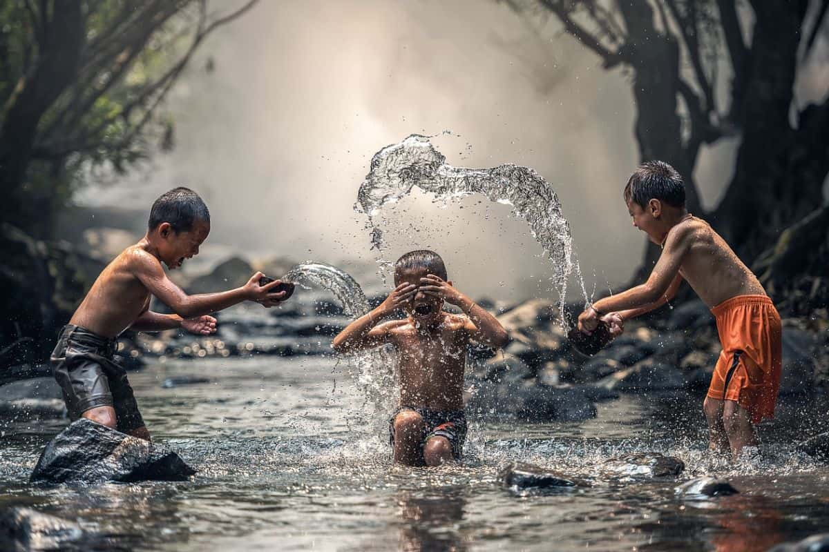 anak-anak yang sedang bermain di sungai sambil tertawa