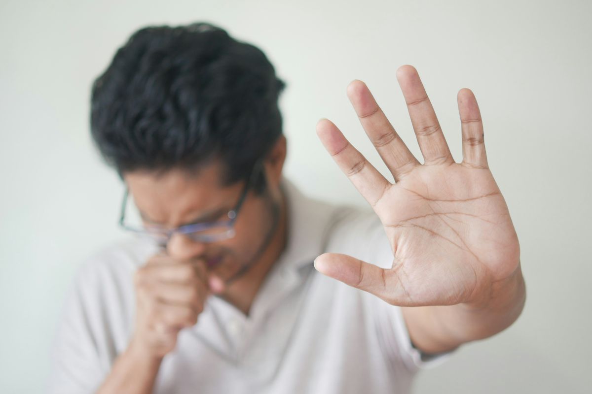 orang yang batuk sambil mengangkat tangan ke depan