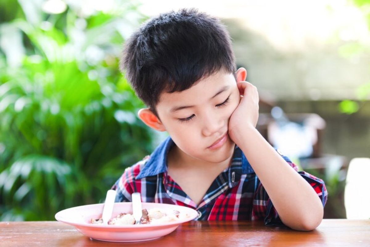 Anak laki-laki berpangku dagu di depan sepiring makanan