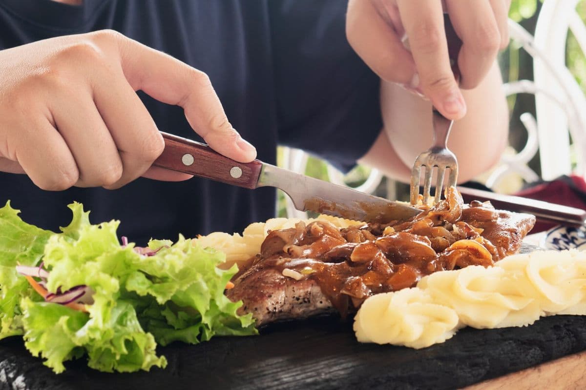 Seseorang sedang makan daging tinggi protein