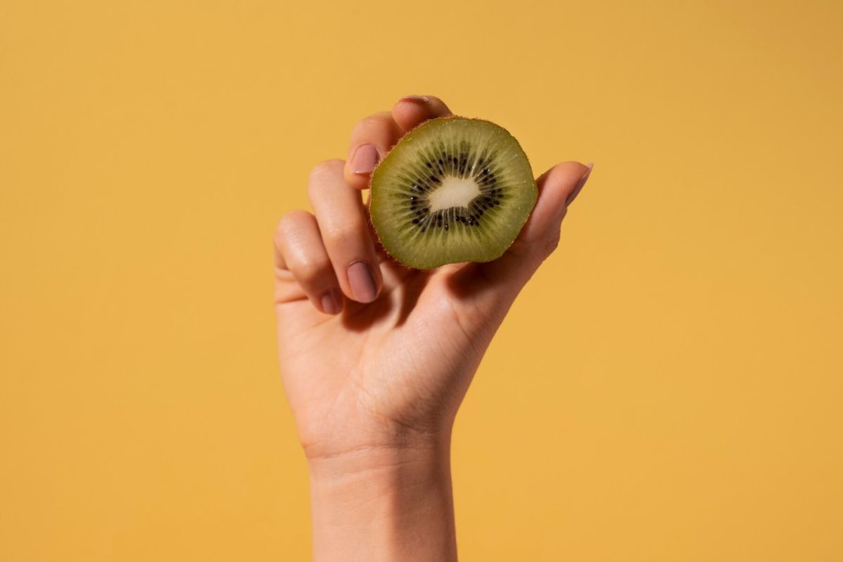 Tangan memegang potongan buah kiwi