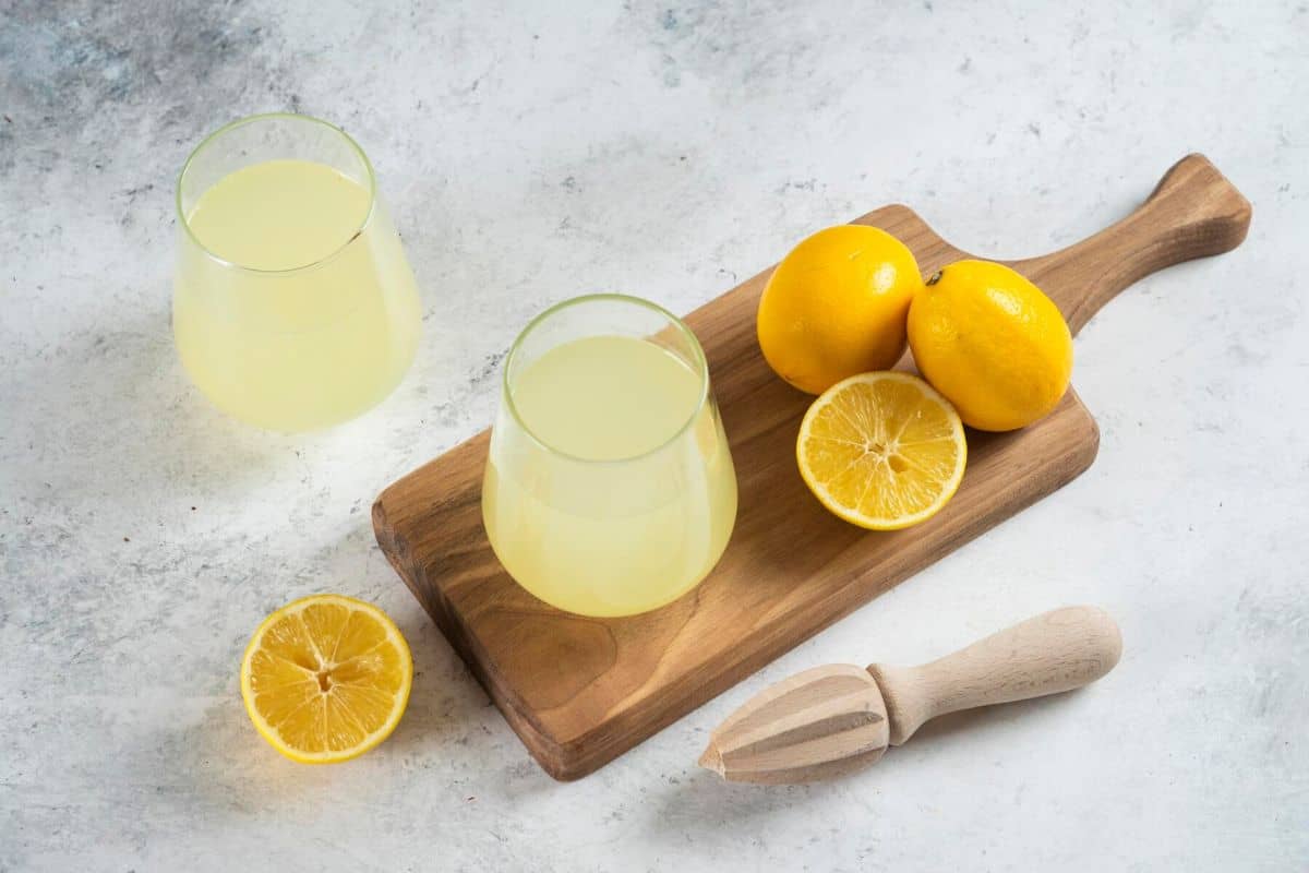 Segelas air lemon dan potongan lemon di atas talenan