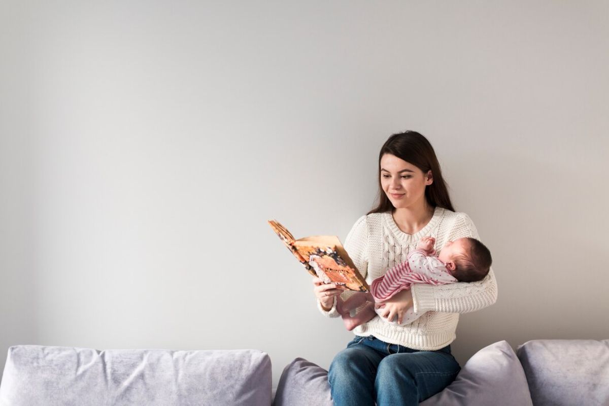 Ibu menggendong bayi sambil baca buku