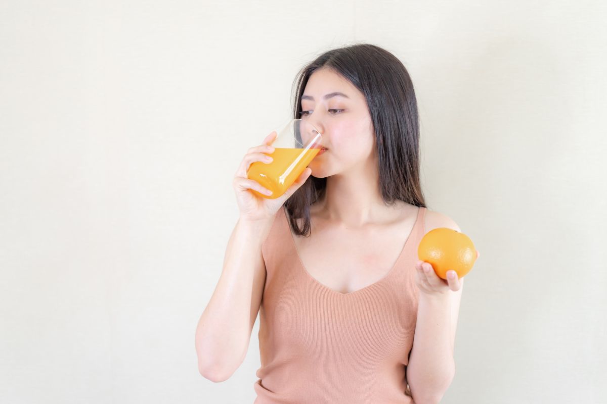 Seorang wanita meminum jus jeruk yang tinggi vitamin C