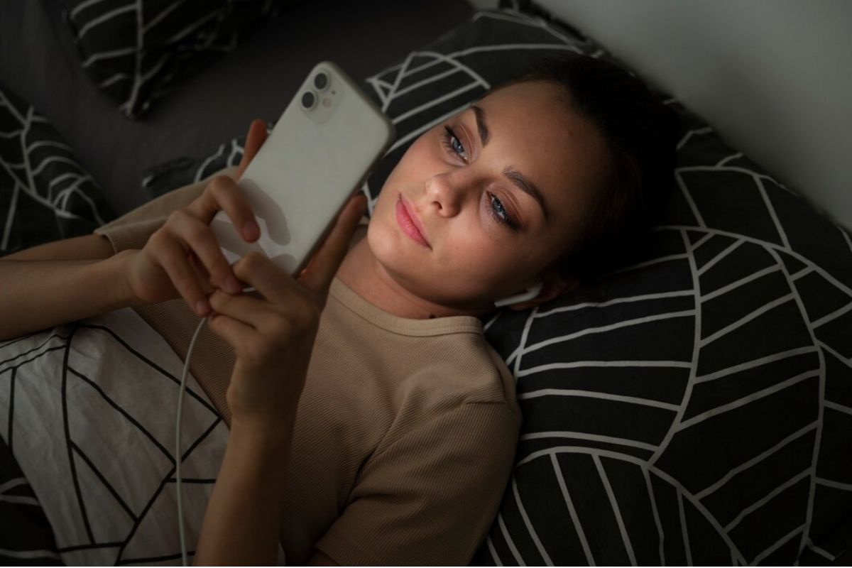 Perempuan bermain smartphone di tempat tidur