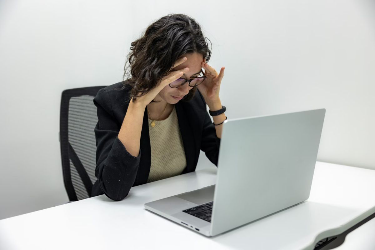 Perempuan memegang kening di depan laptop