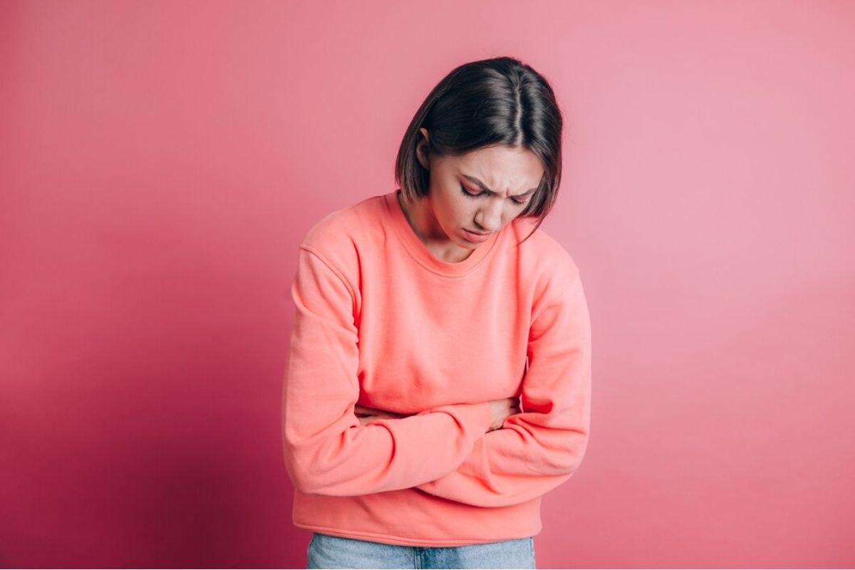 Perempuan menggunakan sweater dan memegang perutnya