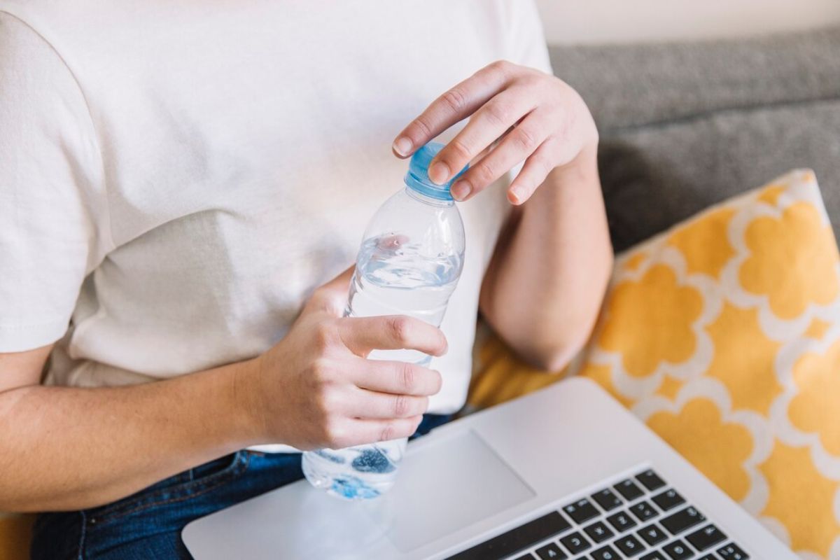 Perempuan melihat laptop sambil membuka botol minum