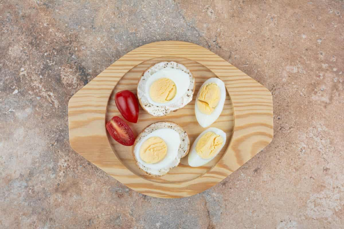 risan roti dengan telur rebus dan tomat di piring kayu