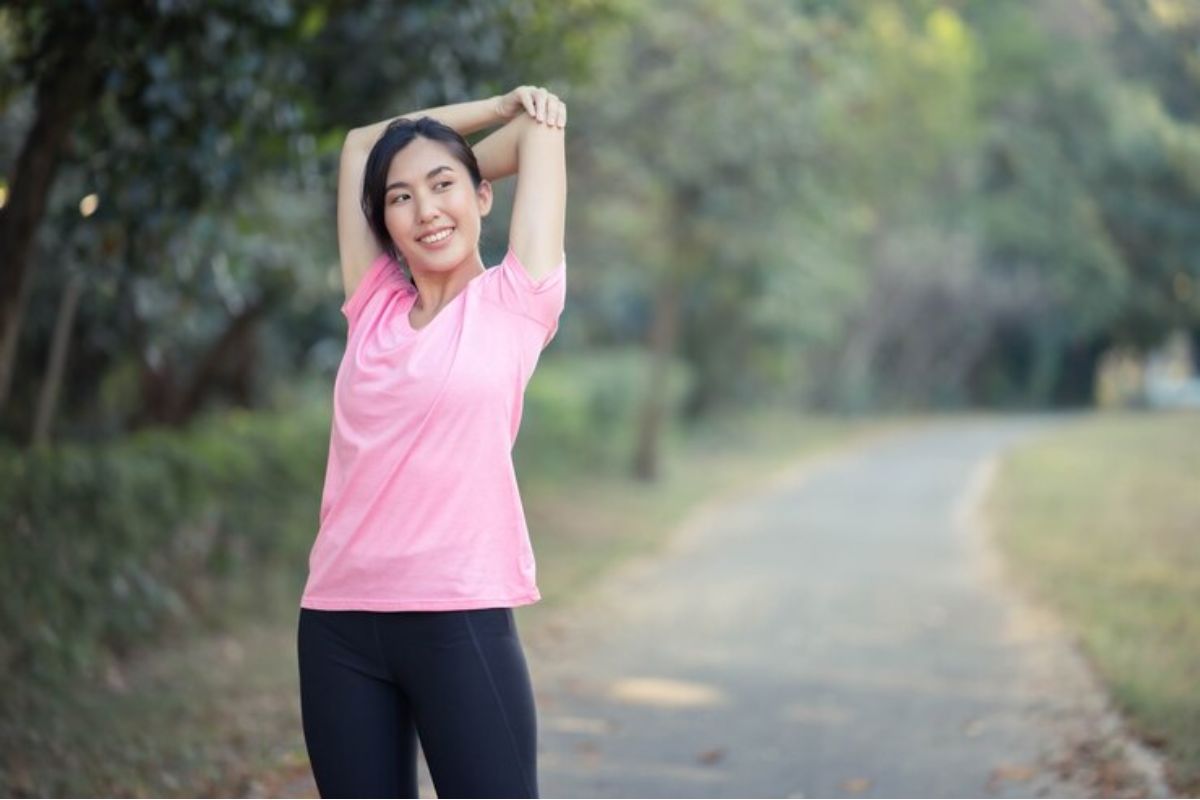 Seorang perempuan sedang melakukan pemanasan di taman